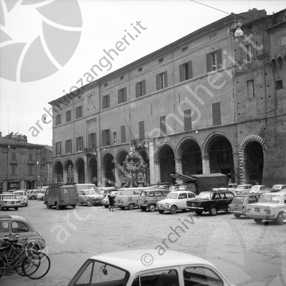 Piazza del popolo con auto parcheggiate vista fontana Masini e palazzo del comune Palazzo Albornoz camion furgoni biciclette auto parcheggiate archi e portici Bianco magic