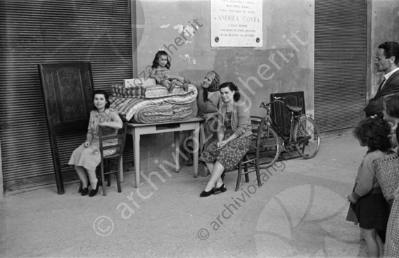 Sfratto Donne e bambina con mobilia sotto i portici del comune Madre mamma bambina nonna tavolo sedie bicicletta Andrea costa materassi