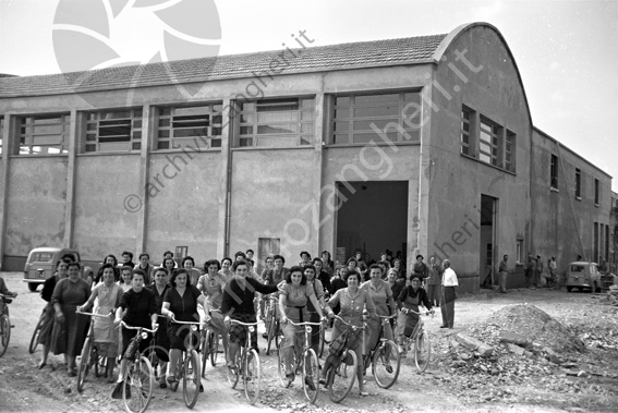 Magazzino Bianchi gruppo operaie in uscita in bici capannone donne lavoratrici