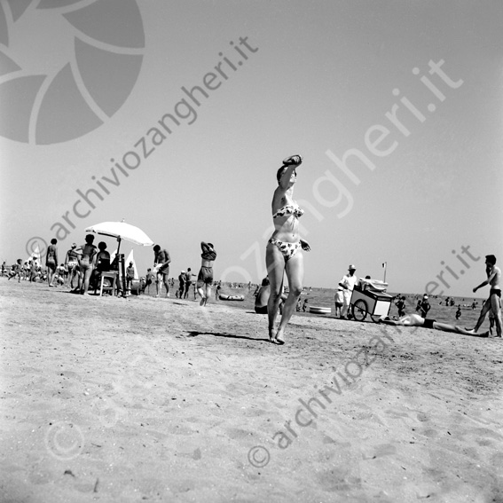 Ragazza in spiaggia Ragazze in costume da bagno mare riva spiaggia bagnanti estate prendere al volo l'anello ombrellone carretto venditore ambulante