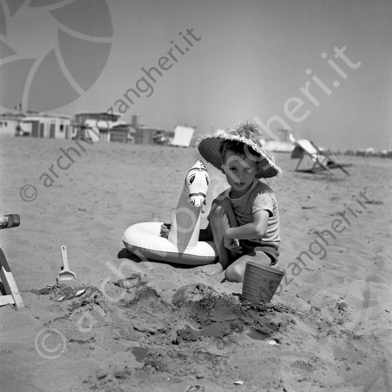 Bambino con salvagente in spiaggia Ciambella cavallino paletta secchiello spiaggia sabbia